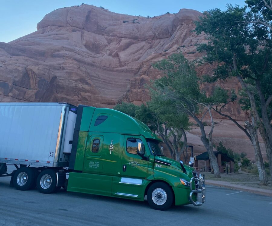 A green freight transport truck pulling a white trailer parked at Hole in the Wall, Utah