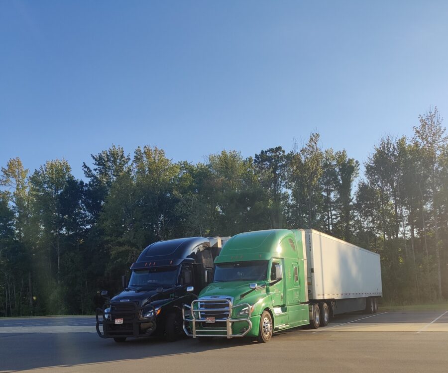 A black and a green semi truck next to each other in front of trees