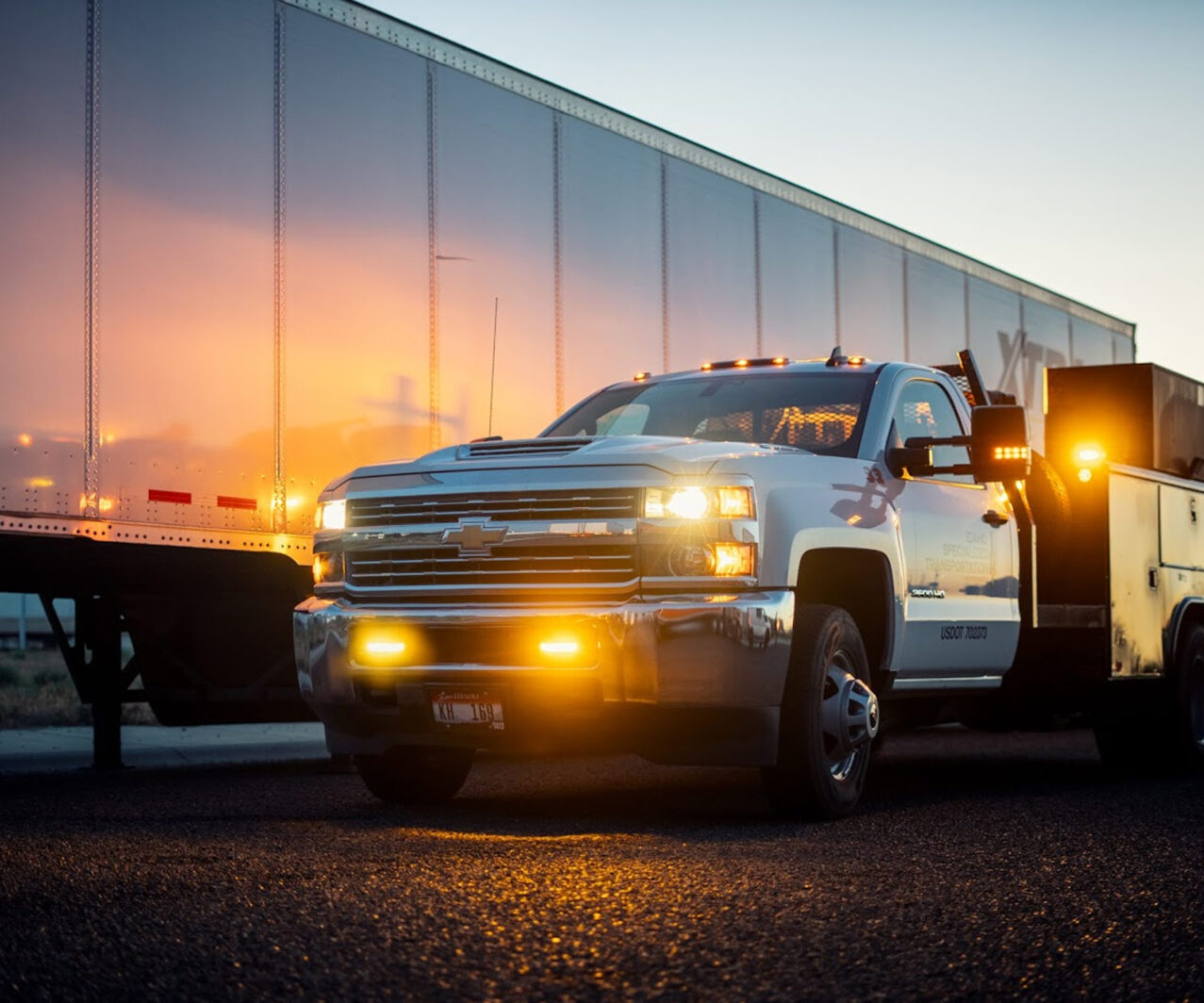 A white Chevrolet pickup truck parked next to a freight trailer at dusk
