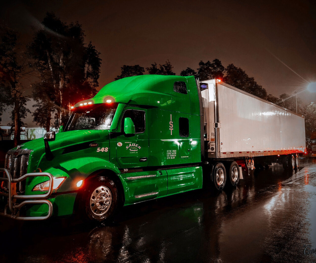 A green semi freight truck pulling a white trailer at night